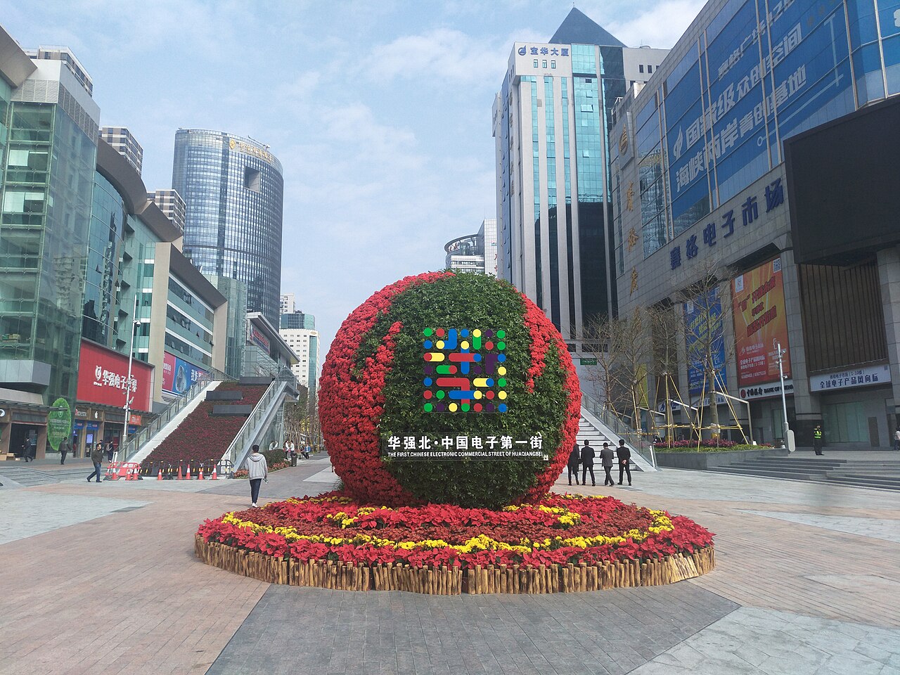 The entrance of Huaqiangbei electronics district in Shenzhen, with a large decorative sphere bearing the district logo, surrounded by electronics markets and high-rise buildings