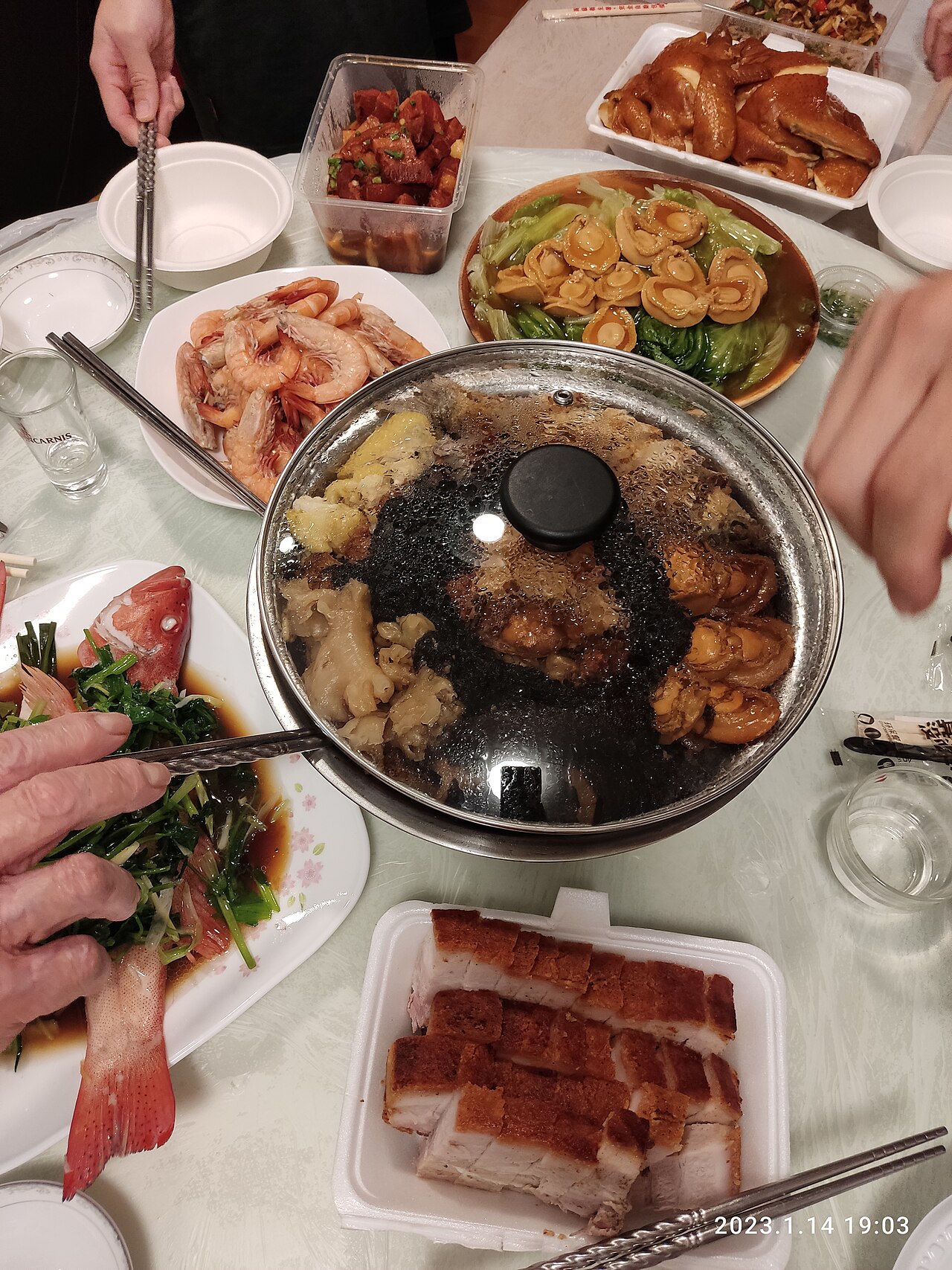 Chinese New Year reunion dinner with hot pot at center, surrounded by dishes of shrimp, roast pork, and other shared plates on a round table