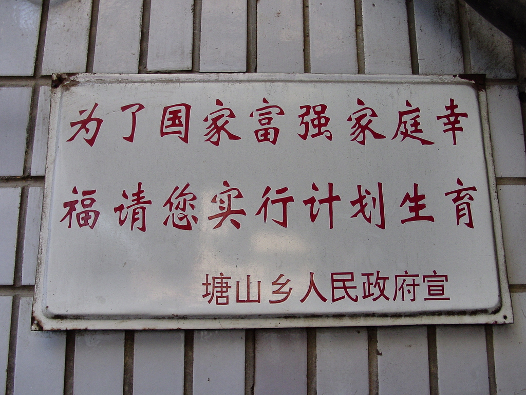 A white metal sign with red Chinese characters promoting family planning, mounted on a tiled wall in a Chinese township