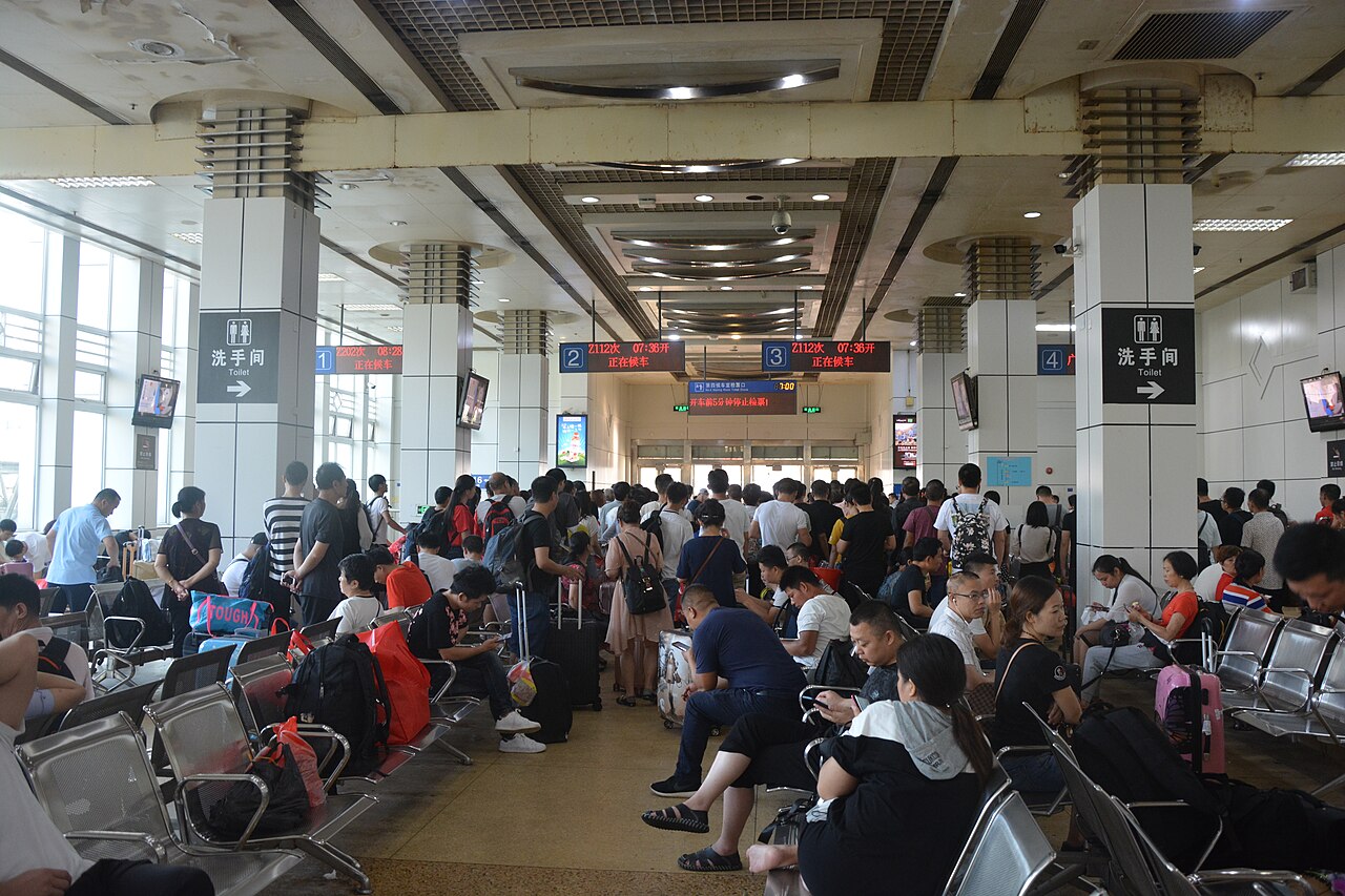 Crowded waiting hall at Guangzhou Railway Station with passengers sitting and standing near departure gates, Chinese signage overhead