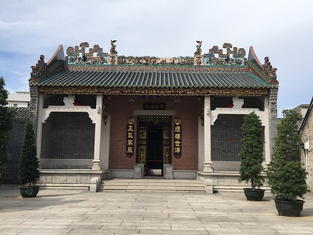 Traditional Cantonese ancestral clan hall in Fenghuang village with ornate ceramic roof decorations, gilded carvings, and Chinese calligraphy on the entrance pillars