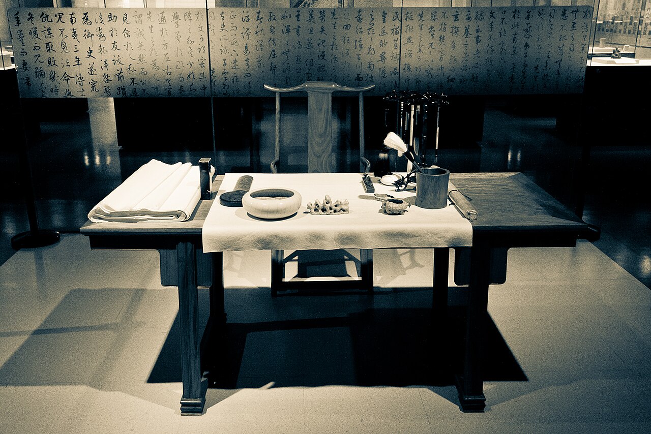 Traditional Chinese calligraphy tools including brushes, an ink stick, rice paper, and a carved inkstone